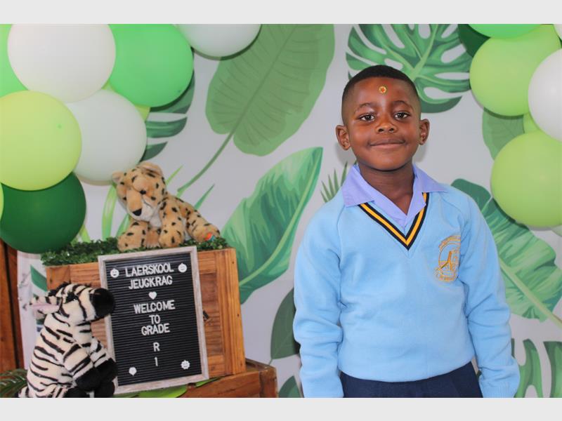 boy in light blue school uniform in front of a wall with leaf motiff