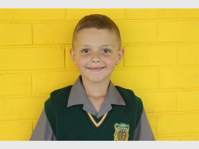 boy in school uniform in front of a yellow brick wall