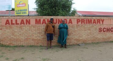 two people in front of the brick wall of a school
