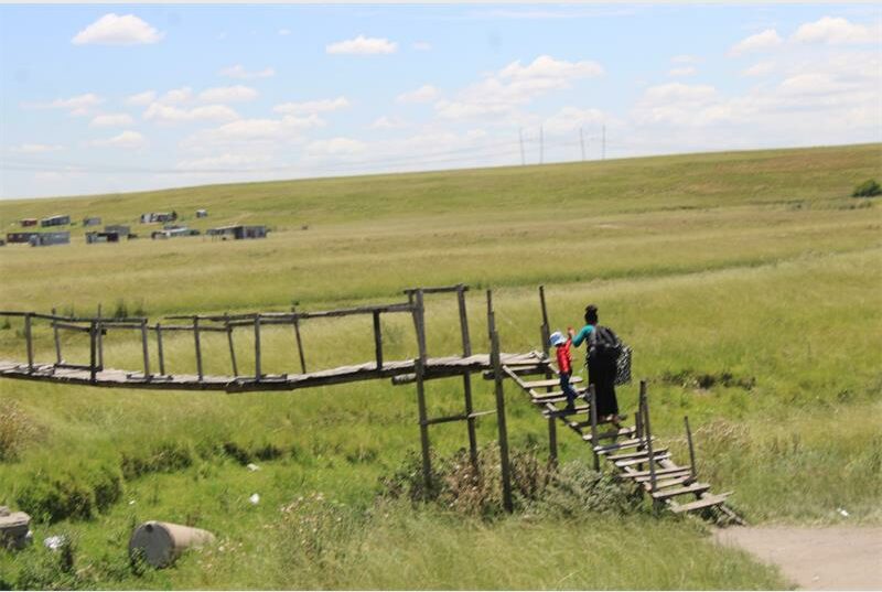 a woman and child scale a wooden bridge across a river
