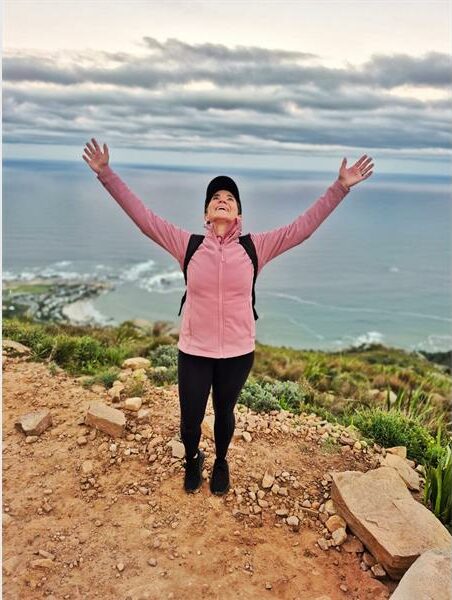 a woman standing on a mountain top lifts up her hands
