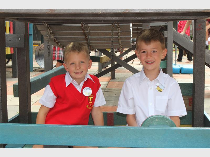 boy with red pull over sits next to boy in white school shirt on a jungle gym