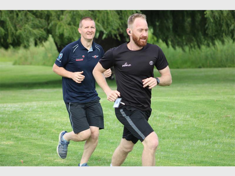 two men dressed in black runs in a park