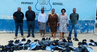 row of people with donated school clothes in front of them on the ground. A wall behind them is painted blue