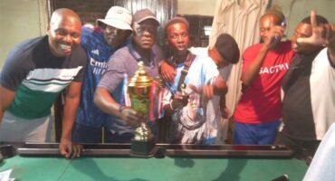 people hold up a cup while standing behind a pool table.