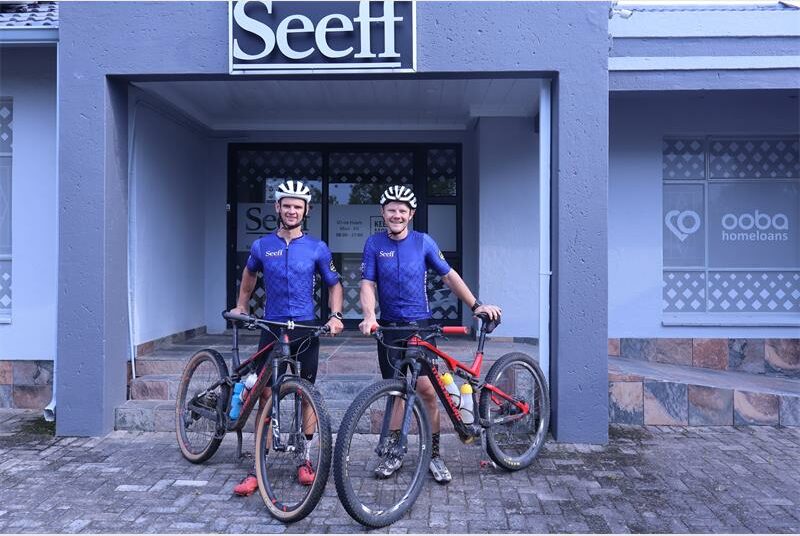 two cyclists in front of a building with the word Seeff on it