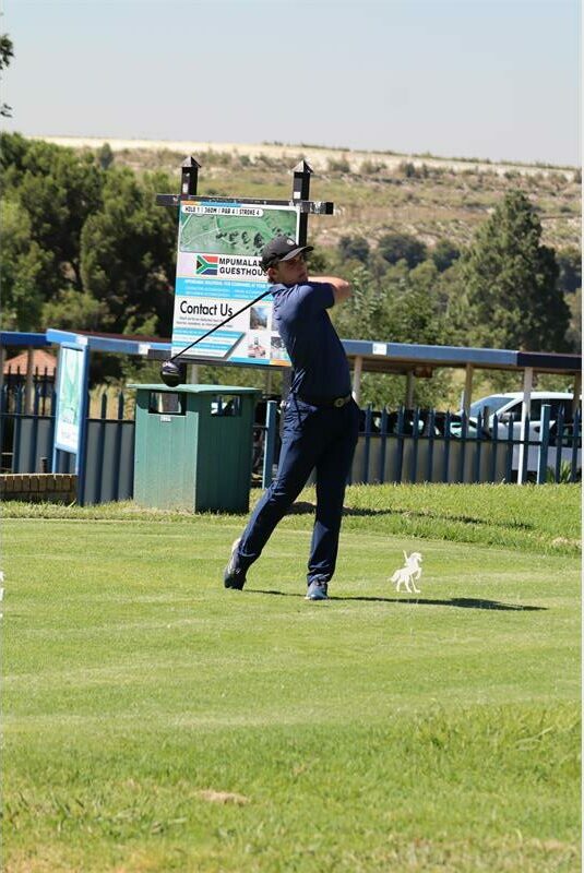 a man in dark blue clothes tees off on the golf course