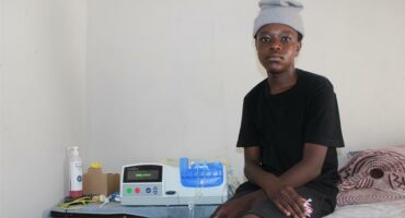 boy sits on bed with a dialysis machine on the bedside table