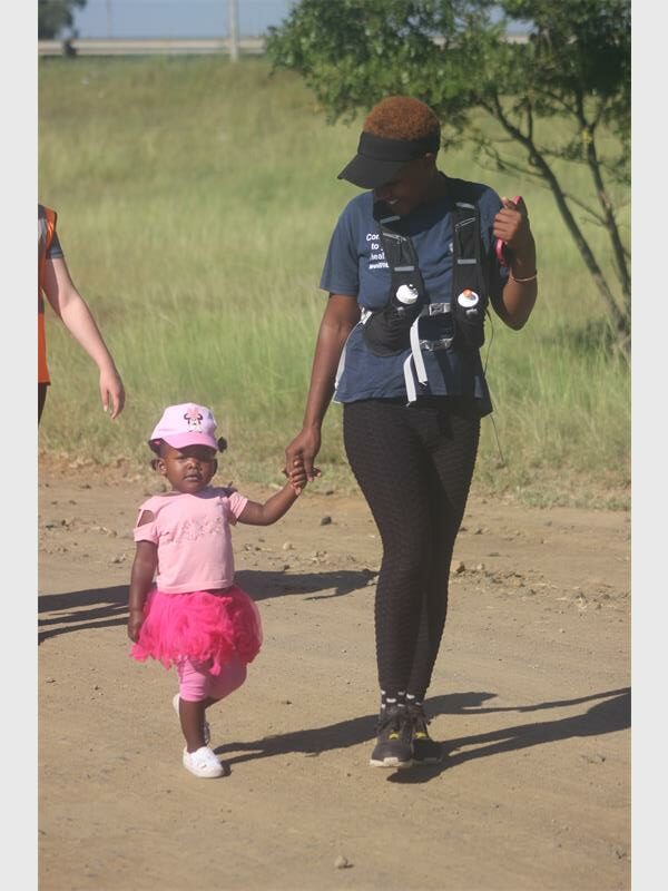 A woman hold the hand of a toddler in pink as they walk on a dirt road