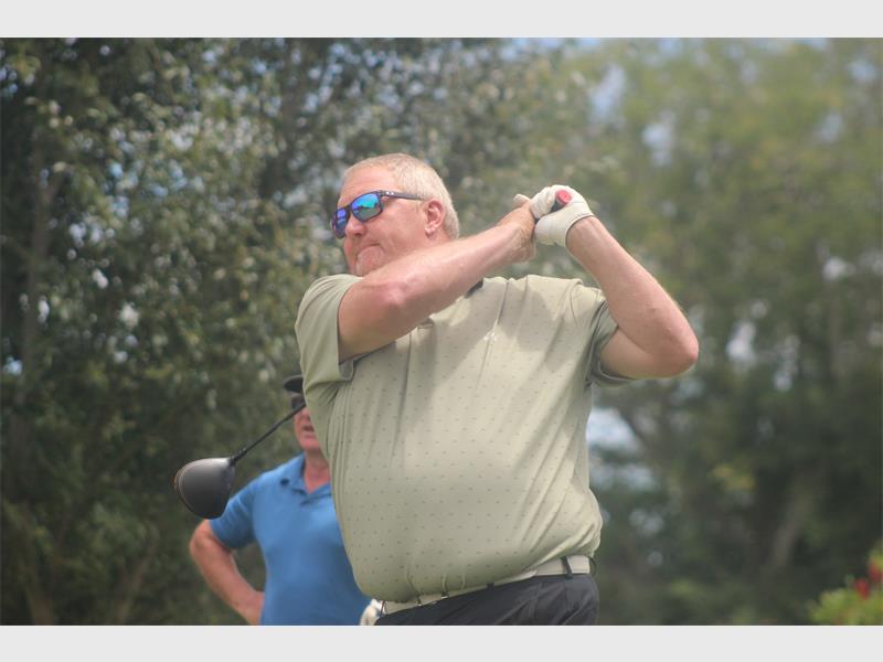 man with beige t shirt hits the golf ball