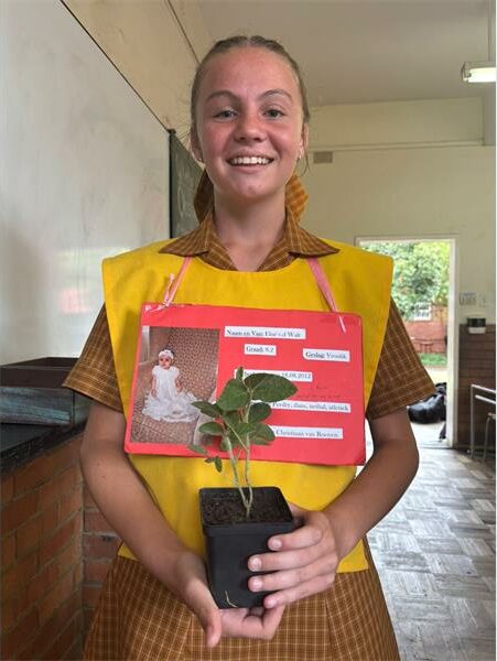 girl with yellow bib holds a small plant in her hands