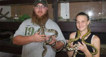 man and woman hold snakes around their necks