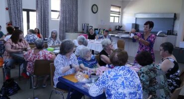women sit at tables, listening to another woman
