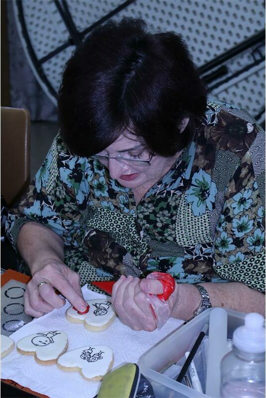 a woman uses red icing o a white heart cookie
