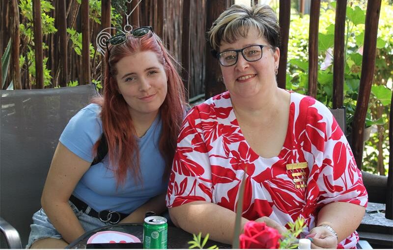 young woman and an older woman with red and white dress sit outside