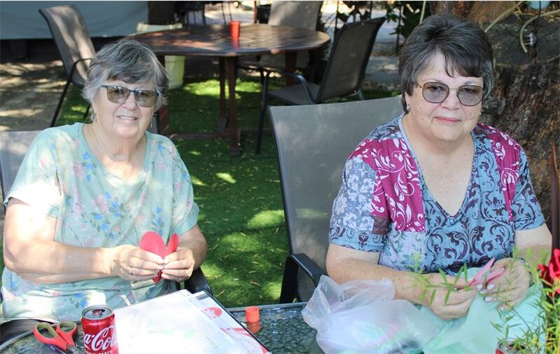 Two women fold hearts at a table outside