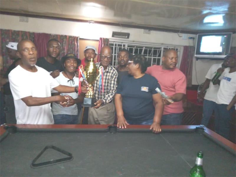 group holds up trophy. There is a pool table in front of them