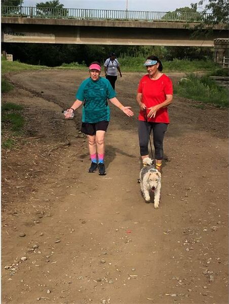 two people with a dog on a dirt road