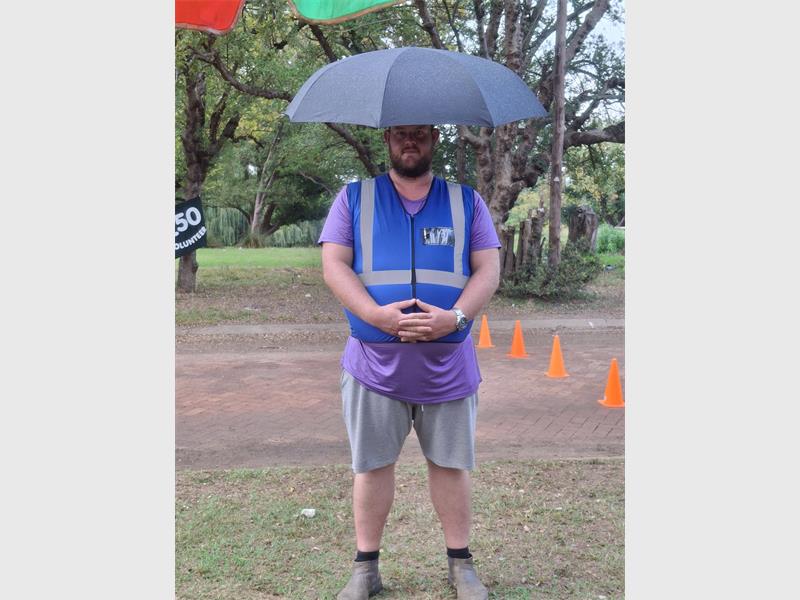 Man with umbrella in a park during rainy weather, wearing casual sports attire.