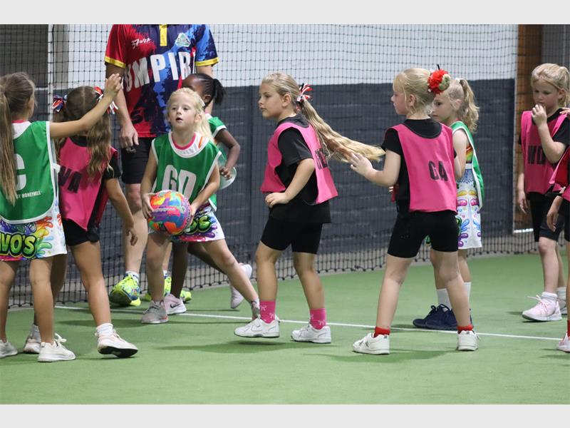 a young girl in green holds onto a netball ball
