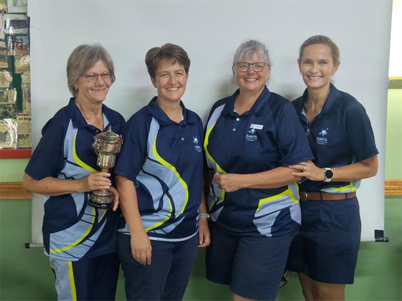 four women in the same sport uniforms. One is holding a trophy