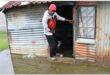 a man stand on a step in the doorway of a sink shack while the ground around him is cobered in sewage