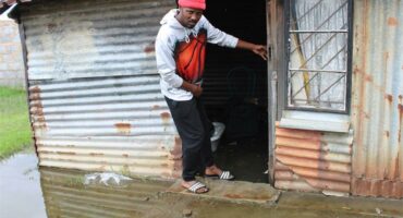 a man stand on a step in the doorway of a sink shack while the ground around him is cobered in sewage