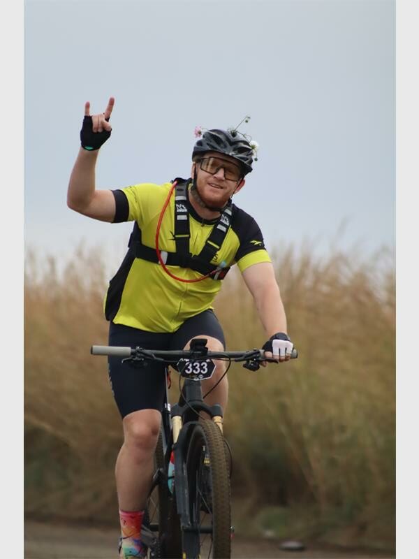a cyclist in a yellow and black outfit signs for the camera