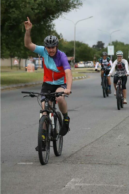 cyclist with red, blue and purple shirt points to the heavens