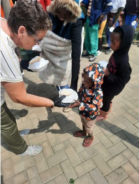 a woman hands a plate of food to a tiny child
