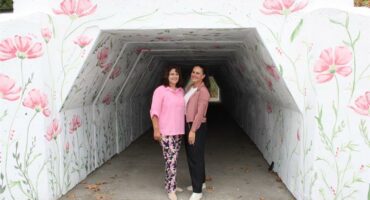 Two women in a tunnel painted white with pink flower