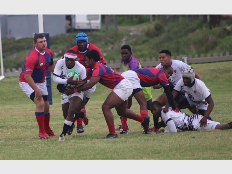 A player in white holding a rugby ball is being tackled by players in red