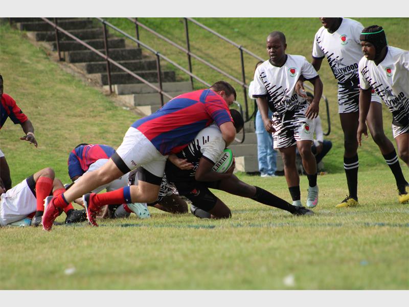 A player in white holding a rugby ball is being tackled by players in red