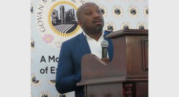 man stands behind a wooden podium with Govan Mbeki Municipality's emblem in the background