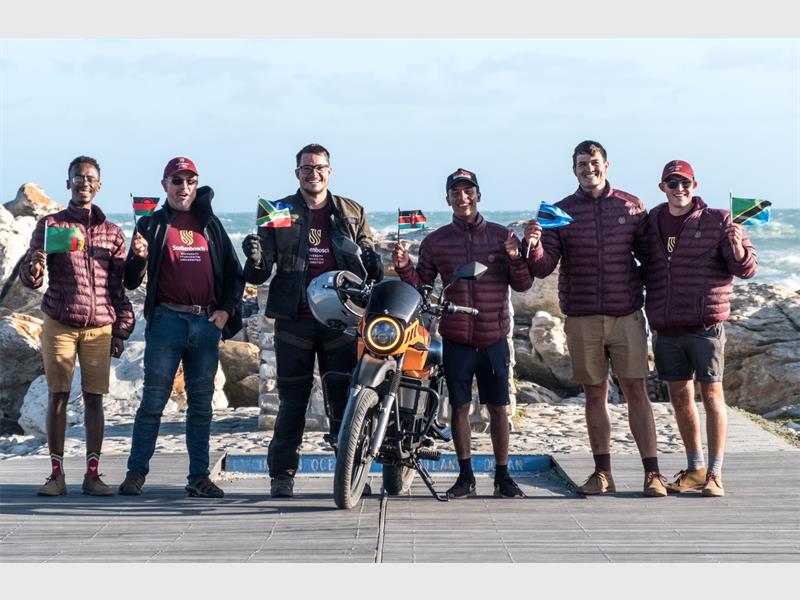 Group of people holding flags at seaside with motorcycle in foreground.