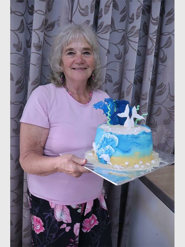 woman holds up a cake with an under the sea theme