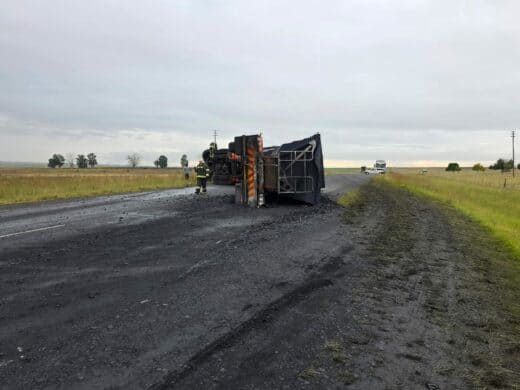 A coal truck on its side in the middle of the road