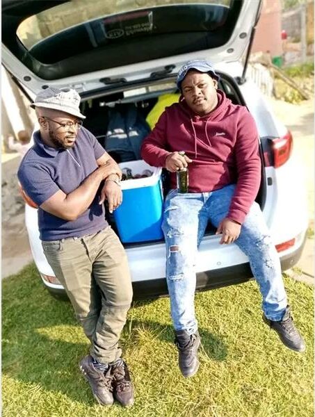 Tow men sitting in the boot of a car with a cooler box and drinks