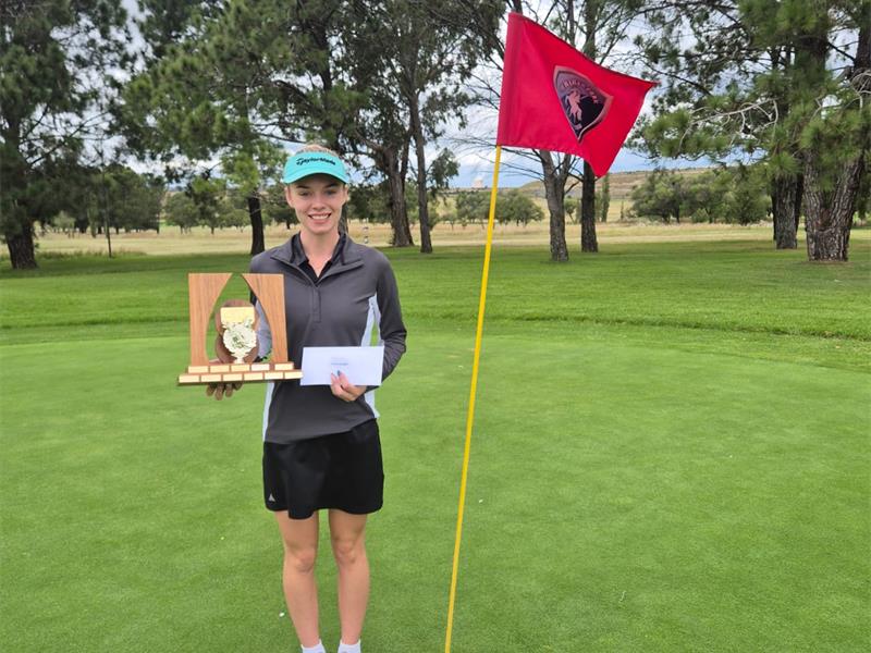 woman with green cap standing on golf green with a large trophy
