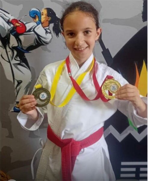 Girl in martial arts gi holding medals after competition victory.