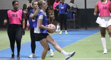 Girls playing netball in pink and blue uniforms during a match.