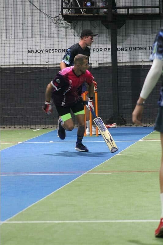 Cricket player running with bat during indoor match at Ridge Times sports facility.