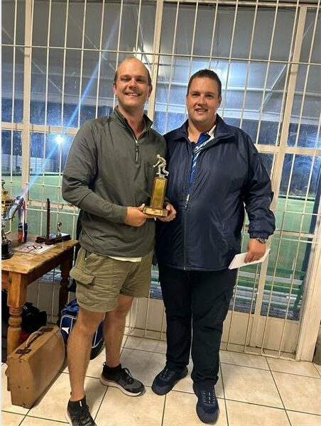 Celebrating victory at Ridge Times with two men holding a trophy indoors.