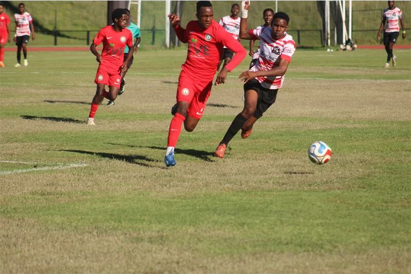 a soccer player in red and a player in a white and red jersey and black pants compete for the ball