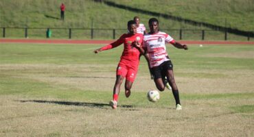 a soccer player in red and a player in a white and red jersey and black pants compete for the ball