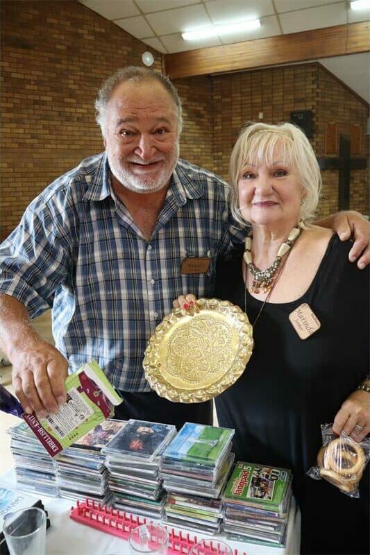 Two smiling individuals holding a decorative plate at a community gathering.
