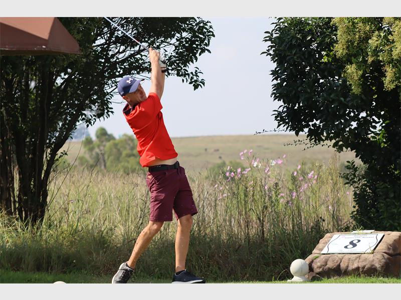 Golf player swinging club outdoors in a grassy field.