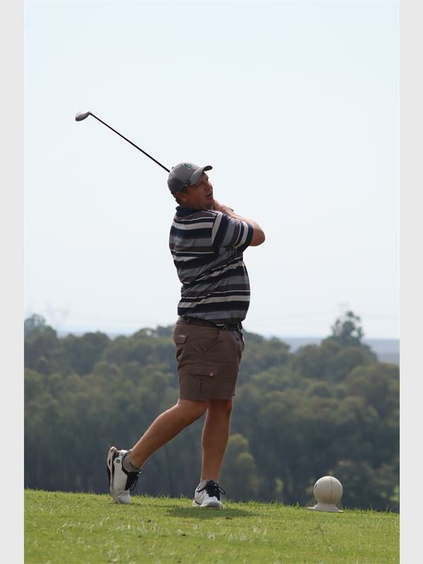 Golf player in mid-swing on lush green course with trees in background.