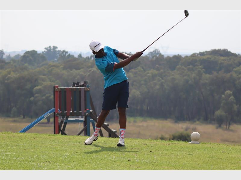 Golf player in action hitting ball with driver on lush green fairway.