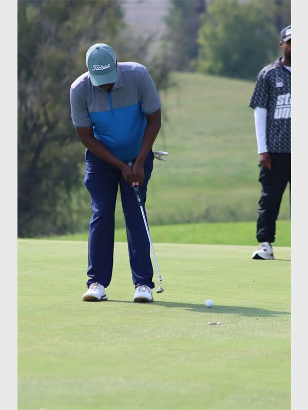 Golf player in blue shirt and cap focusing on the ball.